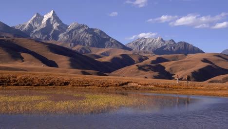 Una-Pareja-Explora-Caminar-A-Lo-Largo-De-Las-Orillas-Del-Lago-En-Las-Montañas-De-Sichuan-Con-Picos-Impresionantes