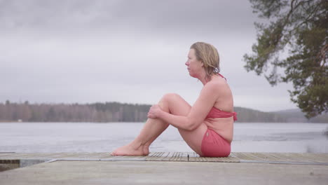 Emotional-and-vulnerable-woman-in-swimsuit-sits-on-lake-pontoon-after-ice-bath