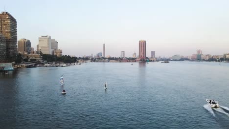 Aerial-perspective-above-the-surface-of-the-Nile-River-in-Downtown-Cairo,-Egypt,-boats-glide-gracefully-along-the-water,-embodying-the-concept-of-maritime-activity-and-urban-vitality