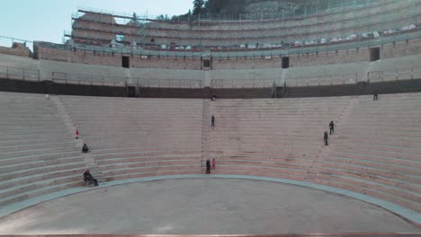 Visitors-on-the-ancient-stage-of-Roman-Theatre-of-Orange-in-Vaucluse,-France---aerial-ascend