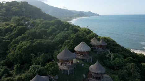 Toma-Aérea-De-Drones-Sobre-Las-Pequeñas-Cabañas-De-La-Selva-Tayrona-Con-Vistas-Al-Océano-En-Colombia.