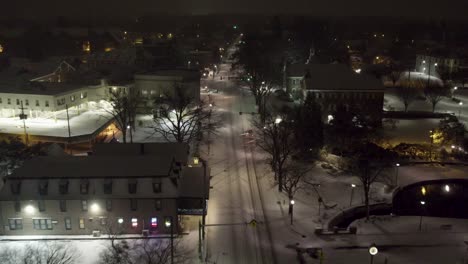 Aerial-shot-following-a-car-above-a-snowy-road-in-downtown-Lititz-at-night,-going-south