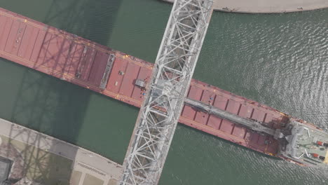 Top-Down-Aerial-of-Cargo-Ship-Passing-Under-Aerial-Lift-Bridge-in-Duluth,-Minnesota