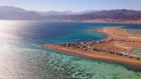 The-aerial-perspective-of-a-blue-lagoon-in-Dahab,-Egypt,-presents-breathtaking-vistas-of-the-adjacent-desert-terrain,-ensuring-visitors-an-unparalleled-and-memorable-adventure