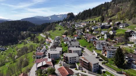 Scenic-swiss-town-with-hotel-apartments-on-hill-with-green-pasture-and-snowy-mountains-in-background