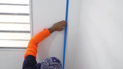 A-Man-is-Placing-Blue-Masking-Tape-on-the-Wall-to-Ensure-that-the-Painting-Lines-are-Clean-and-Precise---Close-Up