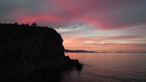 Fliegen-Neben-Einer-Felsigen-Klippe-Im-Meer-Bei-Sonnenuntergang-In-Baja-California,-Mexiko