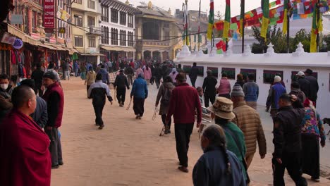 Ground-level-wide-shot-of-Buddhist-Monk-watching-people-walk-around-the-outer-section-of-Boudhanath-Temple,-Kathmandu,-Nepal