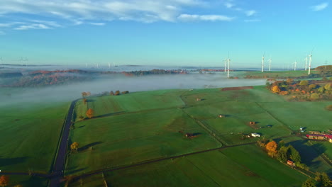 Aerial-View-of-Picturesque-Landscape-of-Germany,-Green-Countryside-Farming-Fields,-Wind-Turbines-and-Fog-on-Sunny-Autumn-Day