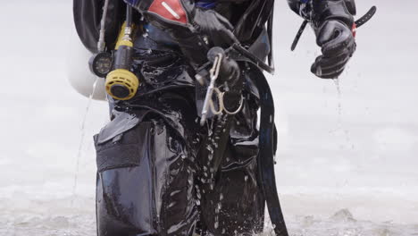 Water-drips-off-dry-suit-and-dive-gear-of-ice-diver-emerging-from-lake