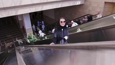 Bespectacled-Muslim-woman-savoring-the-ride-on-an-escalator-in-a-shopping-mall