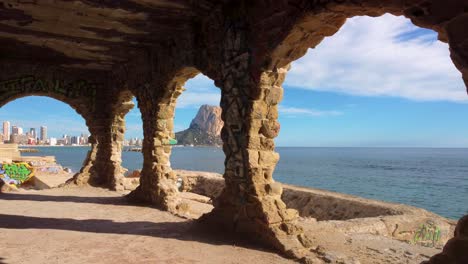 Dramatic-FPV-Drone-View-of-Calpe-Spains-Iconic-Mountain-and-Coastline-Peñon-d'Ifach---also-known-as-Calpe-Rock:-Through-Graffitied-Circular-Windows-in-an-abandoned-graffiti-building