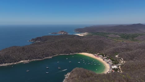 Drone-view-of-Playa-El-Maguey,-a-beach-with-green-colors-and-calm-waters-in-Huatulco,-Oaxaca