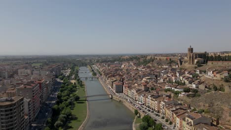 Slow-drone-flight-over-Lleida,-Spain,-along-Rio-Segre-on-a-warm-day