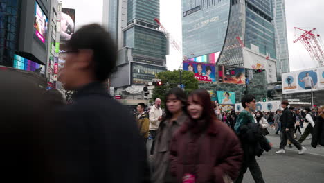 Gente-Cruzando-Y-El-Horizonte-De-La-Ciudad-Durante-El-Día-En-Shibuya,-Tokio,-Japón