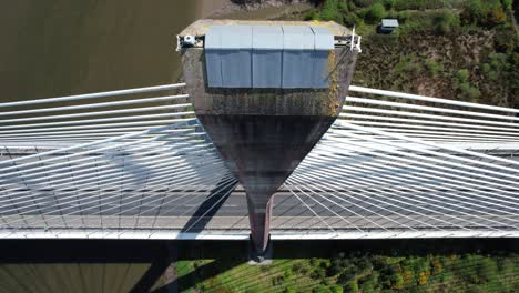 Drone-single-pylon-suspension-bridge-looking-down-from-the-top-of-the-massive-structure-to-the-bridge-below-with-traffic-and-the-river-flowing-through-under-the-bridge-in-Waterford-Ireland