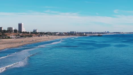 Drone-shot-flying-over-Santa-Monica-beach-with-large-waves-and-busy-beach