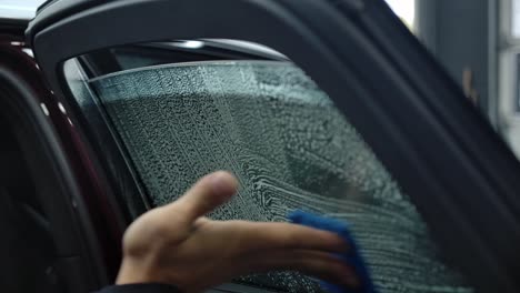 Hand-Uses-Scrubbing-Pad-In-Wiping-Car-Window-With-Cleaning-Detergent-At-Carwash