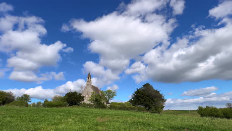 White-fluffy-Cumulus-clouds-passing-over-the-tiny-church-of-St-in-the-Hamlet-of-Weethley,-Warwickshire,-England-in-a-Timelapse-video-on-a-sunny-spring-day