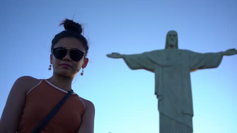 A-woman-in-sunglasses-poses-gracefully-beside-the-breathtaking-sight-of-Christ-the-Redeemer-in-Rio-de-Janeiro,-taking-in-the-magnificence-of-this-iconic-wonder-of-the-world