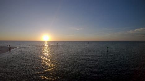 Aerial-4K-Drone-footage-of-the-sun-setting-and-reflecting-over-the-sea-off-Calm-Beach,-in-Naples,-Florida,-USA