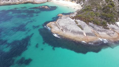Drone-aerial-moving-down-towards-a-secluded-beach-with-white-sand-and-blue-water