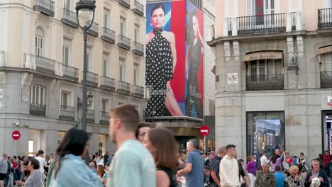 Multitudes-Llenan-La-Puerta-Del-Sol-Con-El-Telón-De-Fondo-De-Un-Cartel-De-Venta-De-Moda-De-El-Corte-Inglés,-Madrid,-España.