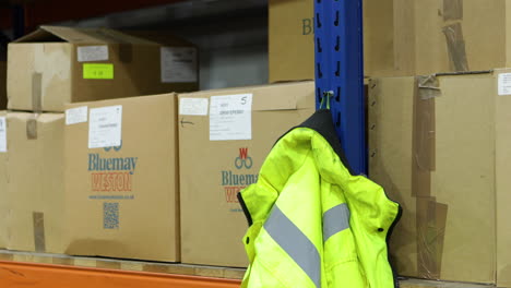 Warehouse-worker-reaches-for-safety-vest-hanging-on-side-of-industrial-shelving