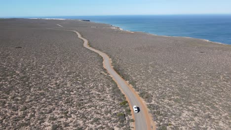 Drone-aerial-pan-up-of-a-van-driving-on-a-country-road-by-a-beautiful-ocean