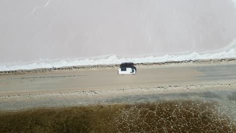 Drone-aerial-over-campervan-driving-slowly-on-road-over-pink-lake-MacDonnell-in-South-Australia