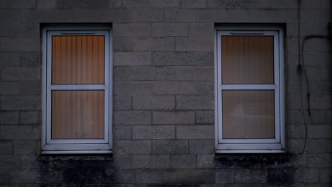 Two-plastic-frame-windows-on-cinder-block-building-facade,-handheld-shot