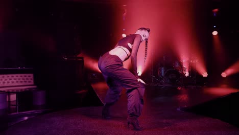 Slow-movement-camera-captures-a-dancer-in-black-pants-and-a-long-braid-dancing-on-stage,-bathed-in-concert-lighting