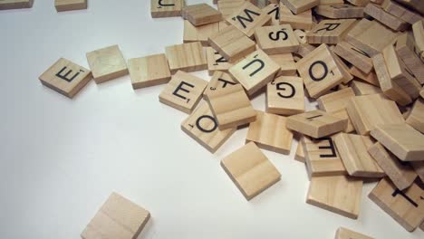 Ein-Stapel-Von-Scrabble-Buchstabensteinen-Tritt-Von-Der-Rechten-Seite-In-Den-Weißen-Rahmen-Ein