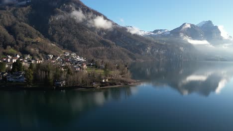 Panning-drone-clip-of-picturesque-Swiss-town-on-edge-of-calm-lake,-on-bright-spring-day-with-blue-skies