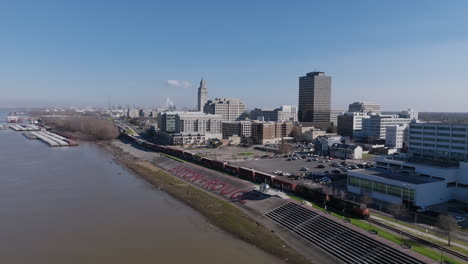 Imágenes-Aéreas-Amplias-Del-Letrero-De-Baton-Rouge-A-Orillas-Del-Río-Mississippi-Con-El-Centro-De-La-Ciudad-Al-Fondo-Y-Un-Tren-Moviéndose-Junto-Al-Letrero.