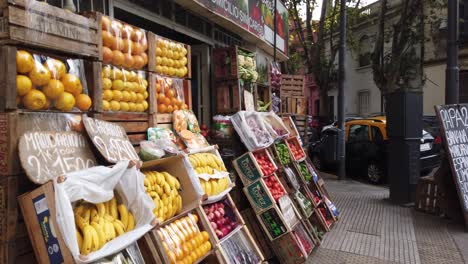 Tienda-De-Frutas-Y-Verduras-Estableciendo-Un-Estante-Colorido-En-El-Mercado-Argentino-Carreteras-De-La-Ciudad-De-Buenos-Aires,-Tráfico-Circulando-Por-El-Fondo