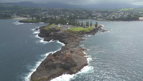Kiama-blowhole-and-lighthouse,-aerial-drone-landscape-long-shot-traveling-along-the-coastal-rocky-headland-and-tourist-spot-at-Pacific-South-Coast