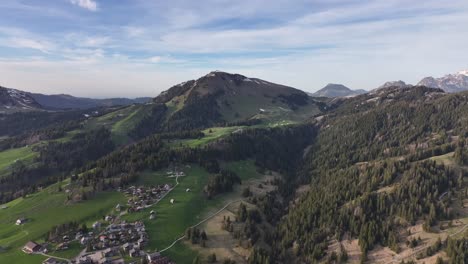 Beauty-of-rural-life-with-this-drone-footage-capturing-majestic-mountains,-tall-trees,-green-grass,-and-charm-of-village-nestled-under-blue-sky-adorned-with-fluffy-white-clouds-at-Amden-Sentis-Schweiz