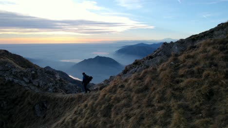 Hiker-walking-at-sunset-on-Resegone-mountain-top-in-Italy-with-breathtaking-views-of-Alps-and-lakes-in-background