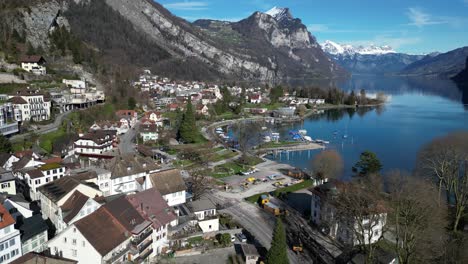 Clip-De-Drone-Que-Muestra-Edificios-Blancos-En-Un-Pequeño-Pueblo-Junto-A-Un-Lago-En-Suiza,-Con-Montañas-Nevadas-Al-Fondo