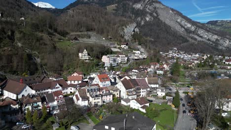 Drone-clip-showing-traditional-white-buildings-in-Swiss-Alps,-next-to-calm-lake,-on-sunny-day-in-Springtime