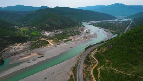 Río-Salvaje-Que-Fluye-Desde-Las-Montañas-En-El-Amplio-Valle-Con-Vegetación,-Agua-Turquesa-Sobre-Un-Hermoso-Fondo-En-Albania