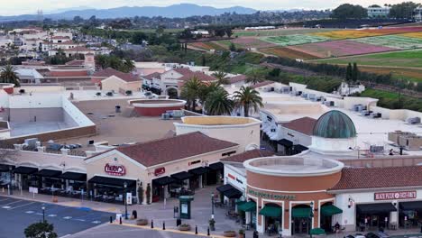 Forward-Motion-Drone-Flight-Carlsbad-Premium-Outlets-to-Southwest-End-of-Mall-Flower-Fields-behind-in-Background-Partial-Bloom-Colorful-stripes-parking-lot-visible