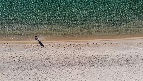 Woman-walking-in-shallow-water-along-a-beach-filmed-with-a-drone