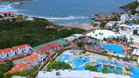 Aerial-views-of-people-on-vacation,-playing-tennis,-in-the-swimming-pool-and-relaxing-by-the-beach-in-Minorca,-Spain