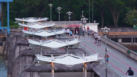 Gesunder-Lebensstil,-Menschen-Fahren-Fahrrad,-Joggen,-Schlendern-über-Den-Stausee-Am-Marina-Barrage,-Dient-Als-Wasserwirtschaftsanlage-Für-Bewässerung,-Hochwasserschutz-Und-Wasserversorgung-In-Singapur