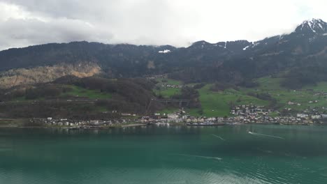 Drone-clip-over-rippled-lake,-showing-Swiss-village-and-cloudy-mountains