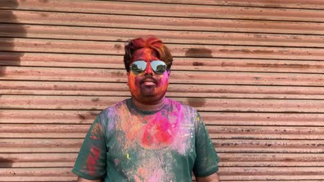 Closeup-shot-of-face-of-a-man-filled-with-colors-wearing-sunglasses-on-holi