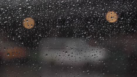 Close-up-shot-of-rain-droplets-with-cars-driving-by-in-the-background