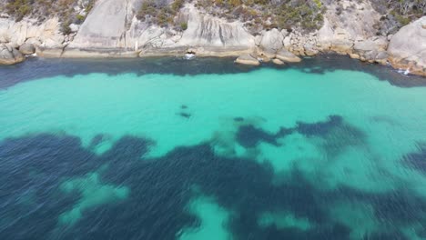 Drone-aerial-moving-back-from-a-blue-watered-coastal-beach-in-Australia